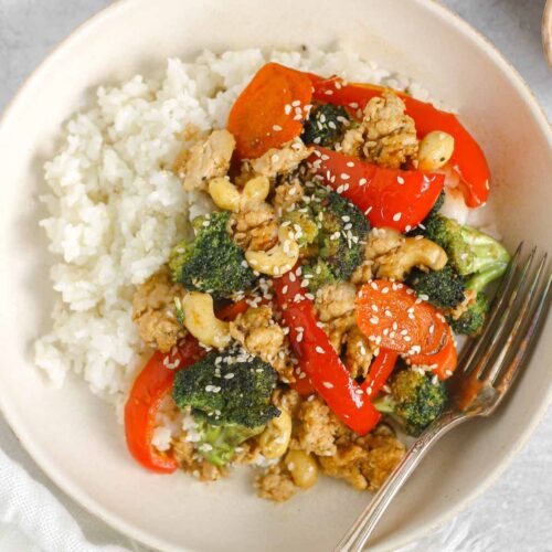 Ground chicken stir fry with veggies and a side of rice in a singe serve shallow bowl with a vintage fork.
