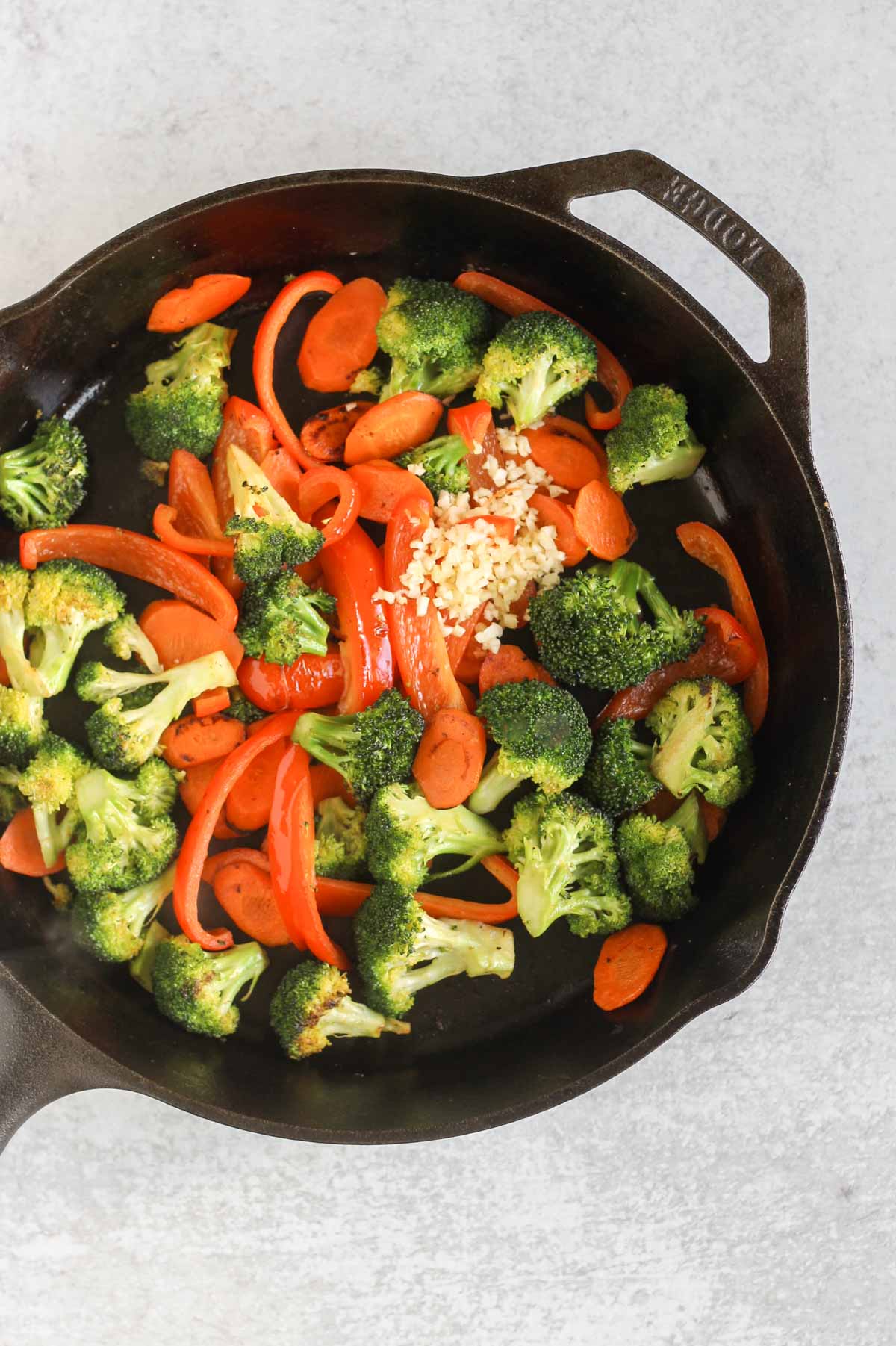 Sautéed broccoli, red peppers, and sliced carrots with fresh garlic and ginger in a cast iron skillet.