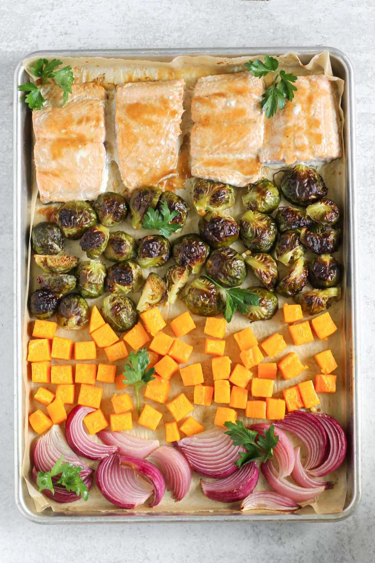 Baking sheet with with cooked salmon fillets, roasted Brussels sprouts, roasted sweet potatoes, and roasted onions.