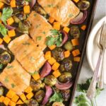 Baking pan with cooked salmon fillets with maple dressing, roasted Brussels sprouts, roasted sweet potatoes, and roasted onions.