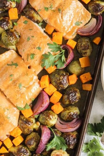 Baking pan with cooked salmon fillets with maple dressing, roasted Brussels sprouts, roasted sweet potatoes, and roasted onions.