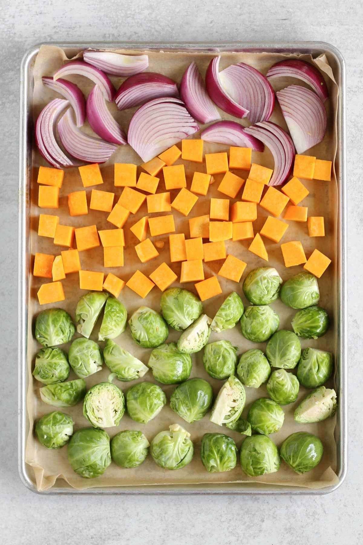 Baking sheet with raw Brussels sprouts, cubed sweet potatoes, and sliced red onions.