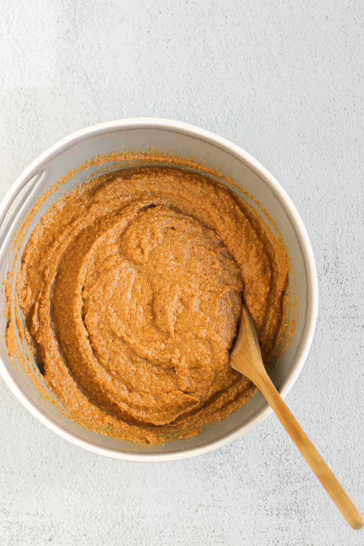 Almond flour pumpkin muffin batter mixed together in a gray mixing bowl with a wooden spoon.