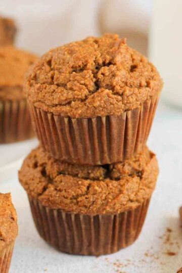 Pumpkin muffins stacked 2 high with extra muffins and a glass of milk in the background.
