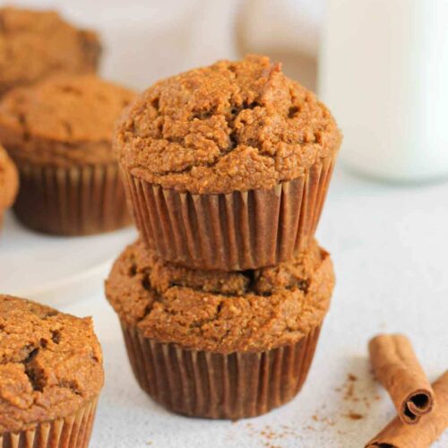 Pumpkin muffins stacked 2 high with extra muffins and a glass of milk in the background.