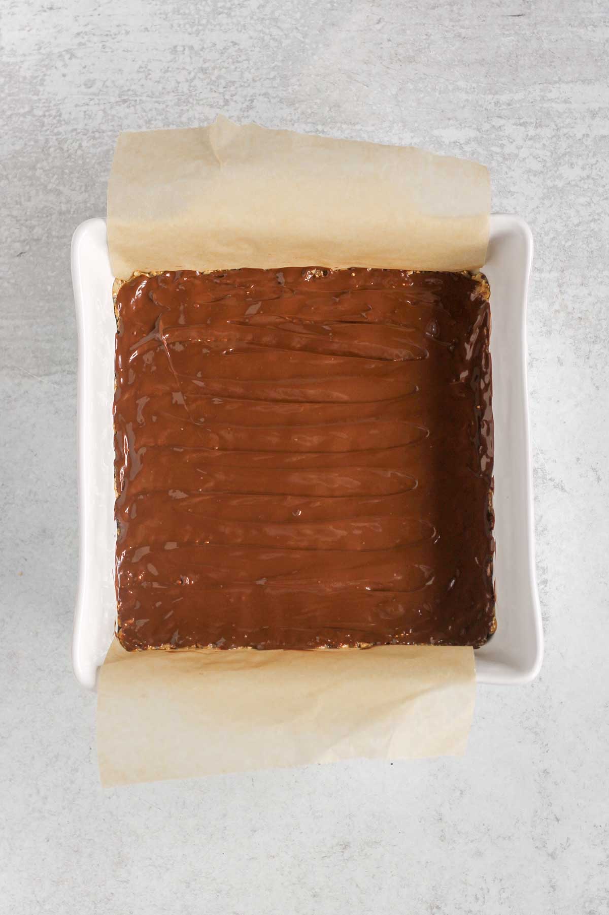 Melted chocolate spread on top of bars in an 8x8 baking pan.