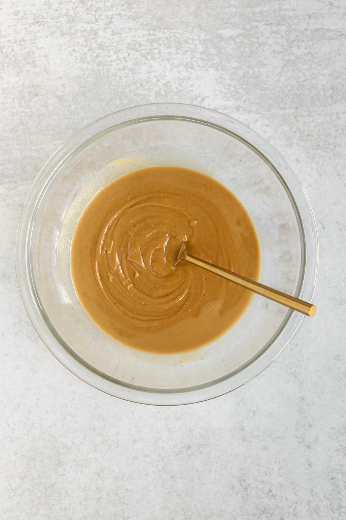 Peanut butter, honey, and oil mixed together in a glass mixing bowl.