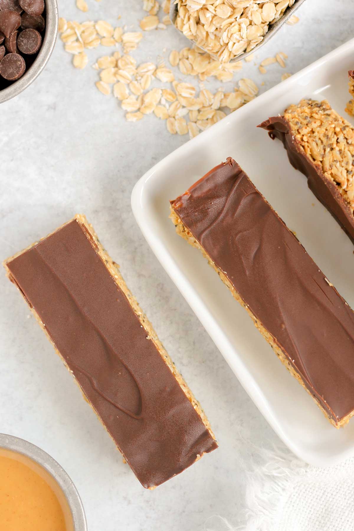 3 chocolate topped granola bars with oats spilt on the side.