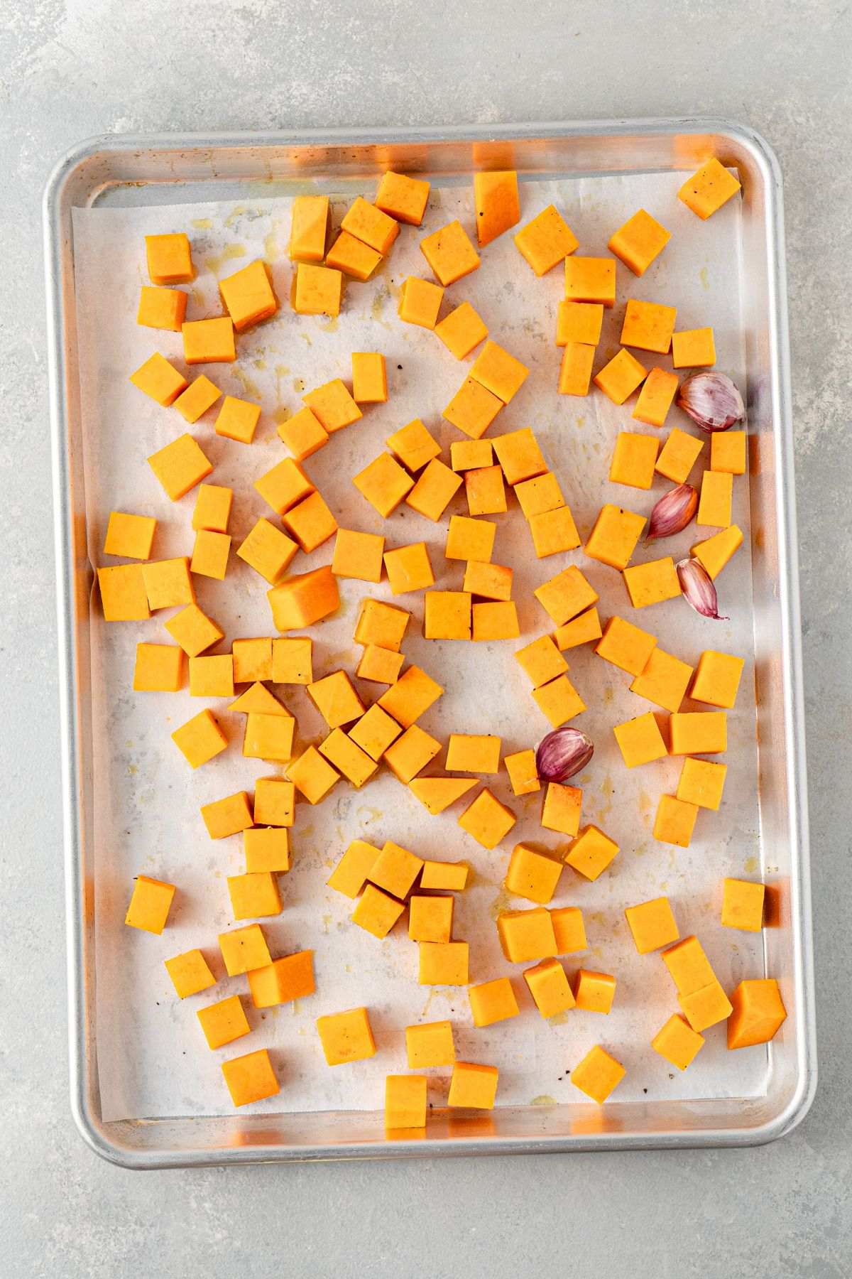 Cubed butternut squash and garlic cloves on a baking sheet.