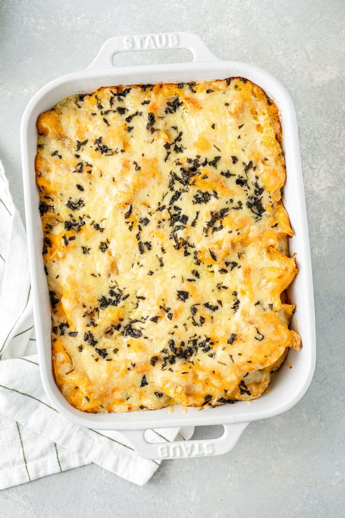 Baked butternut squash mac and cheese topped with melted cheese and chopped sage in a rectangular baking dish.