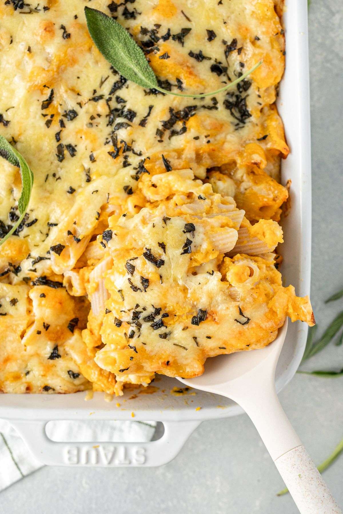 Large spoon scooping out butternut squash mac and cheese from a baking dish.
