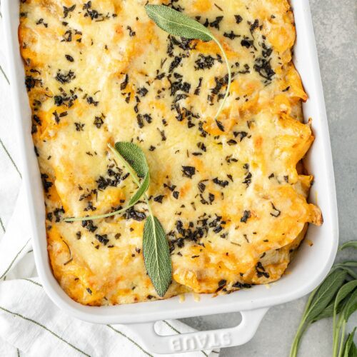 Baked butternut squash mac and cheese topped with melted cheese and fresh sage in a rectangular baking dish.