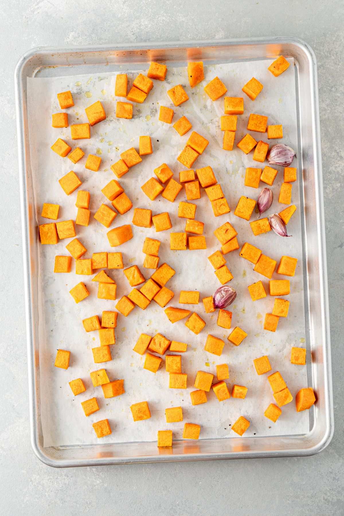 Roasted butternut squash cubes and garlic on a baking sheet.