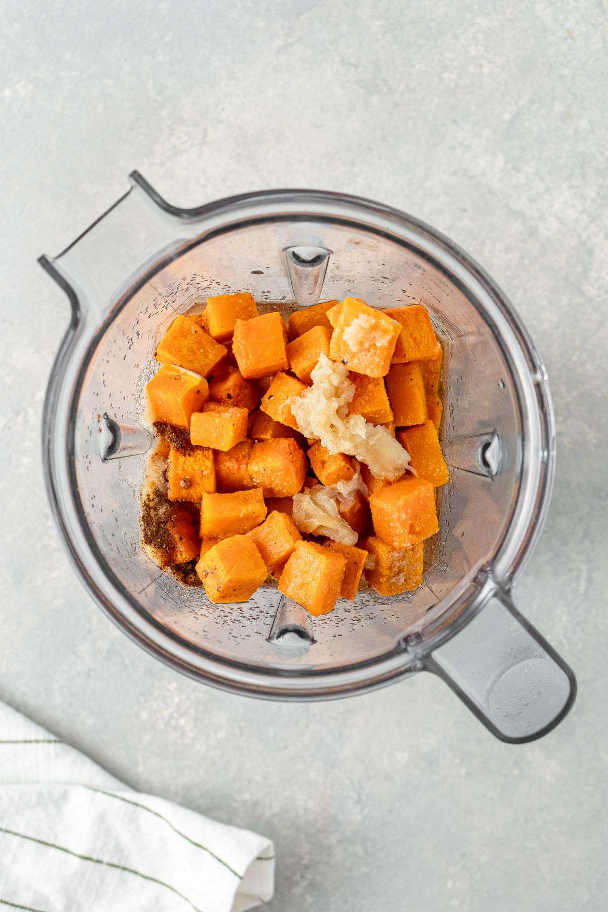 Roasted butternut squash cubes with garlic and seasoning in a blender.