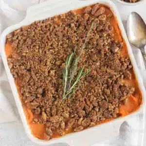 Savory sweet potato casserole topped with pecan crumble and a sprig of fresh thyme and rosemary.