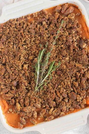 Savory sweet potato casserole topped with pecan crumble and a sprig of fresh thyme and rosemary.
