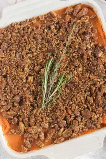 Savory sweet potato casserole topped with pecan crumble and a sprig of fresh thyme and rosemary.