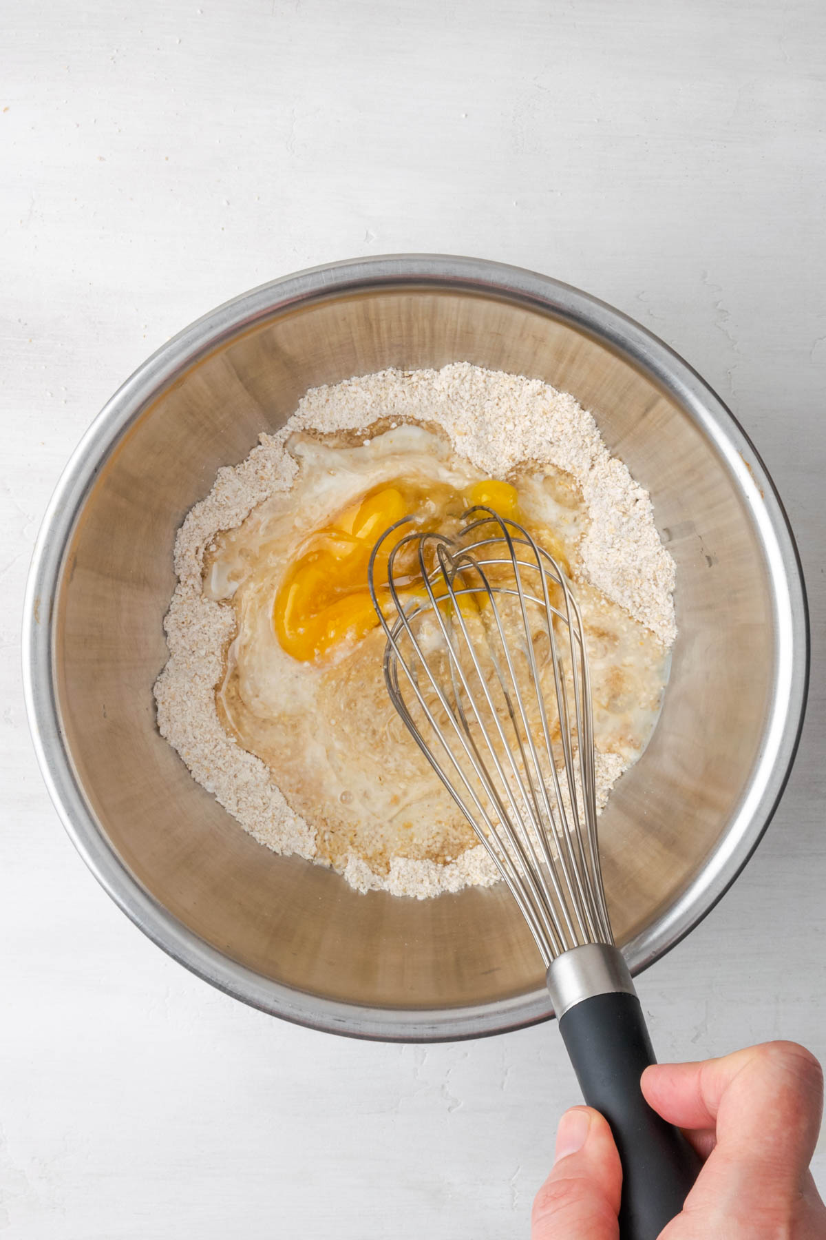 Wire whisk mixing together pancakes ingredients in a mixing bowl.