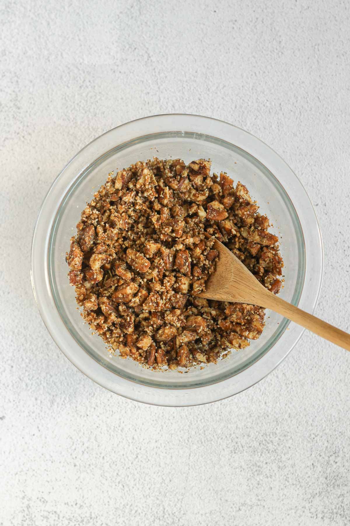 Pecan crumble topping with a wooden spoon in a small mixing bowl.