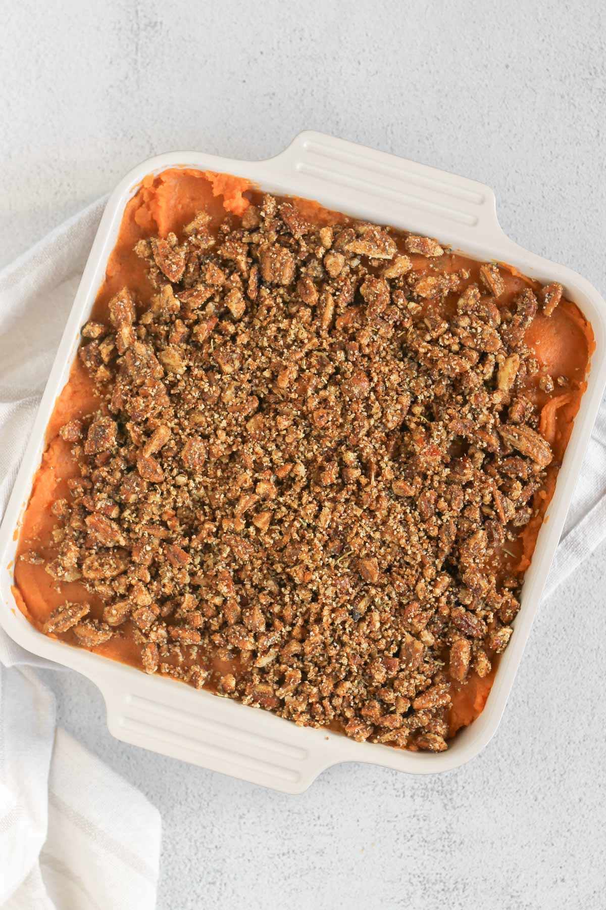 Mashed sweet potatoes sprinkled with pecan crumble in a square baking dish before going in the oven.