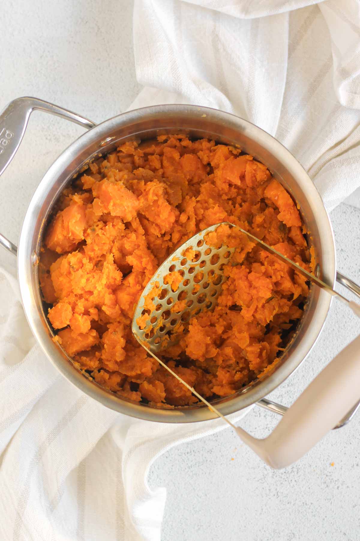 Mashed sweet potatoes with a potato mashed in a stainless steel pot.