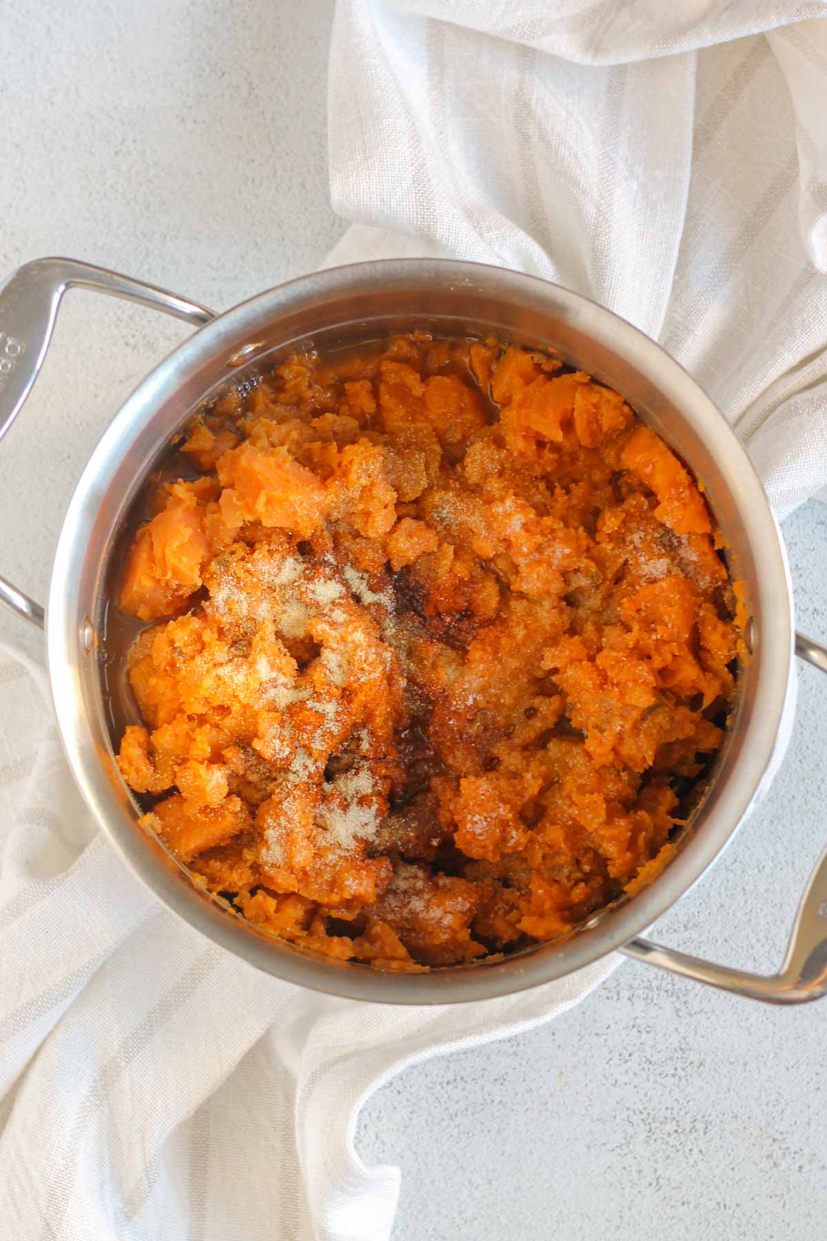 Mashed sweet potatoes sprinkled with seasoning in a stainless steel pot.