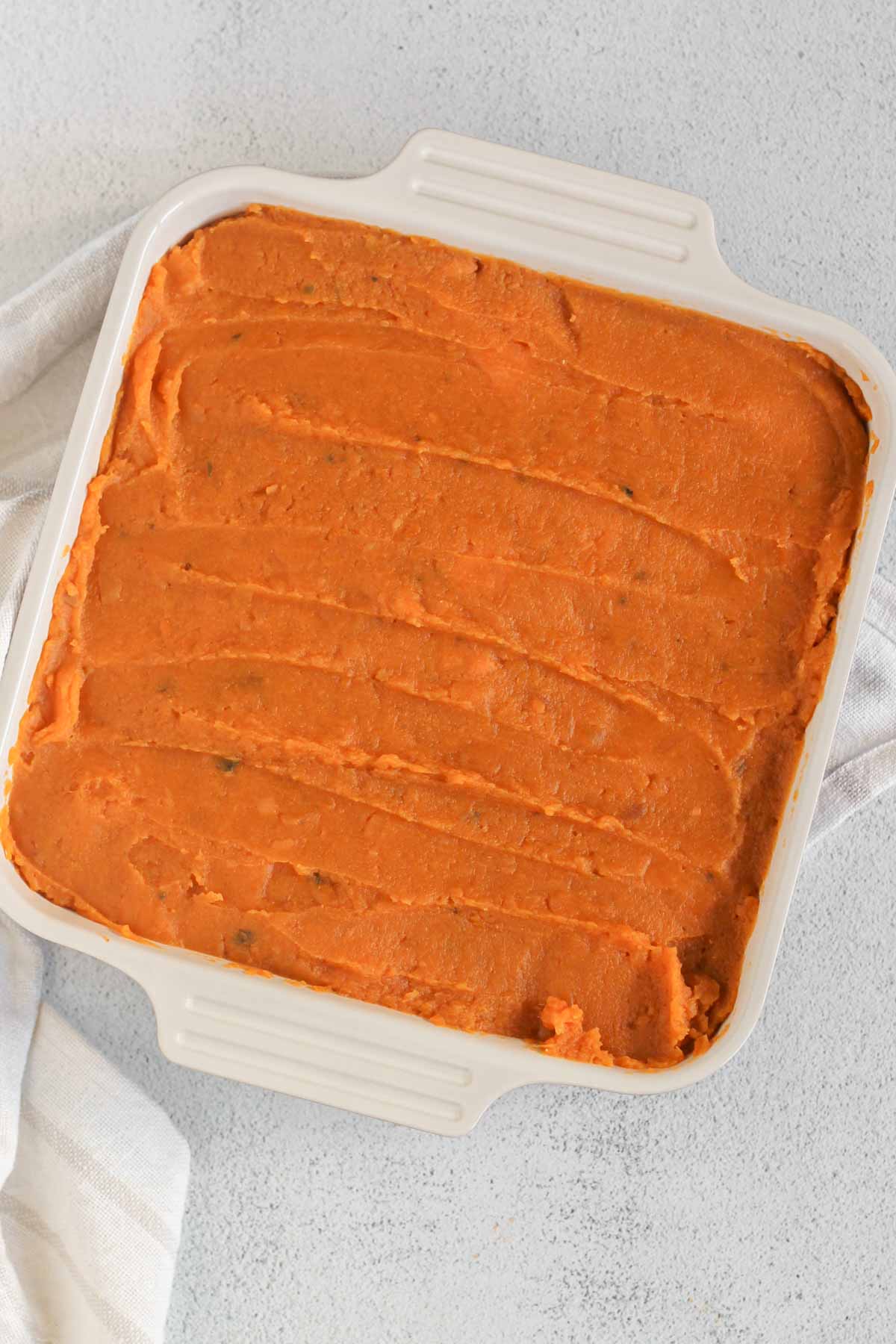 Mashed sweet potatoes spread out in a square baking dish.