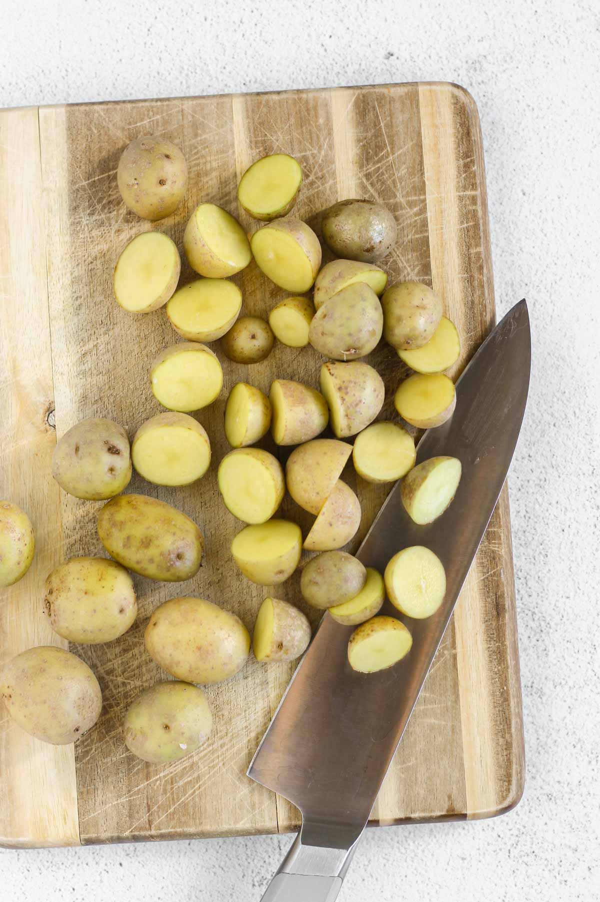 Sliced baby potatoes on a cutting board with a large knife.