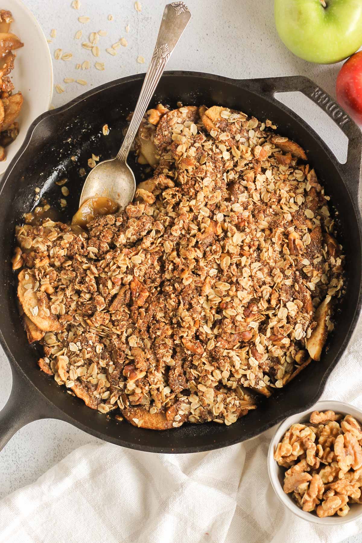 Apple crisp in a cast iron skillet with some taken from the side of the skillet and a serving spoon in the skillet scooping up some of the apples.