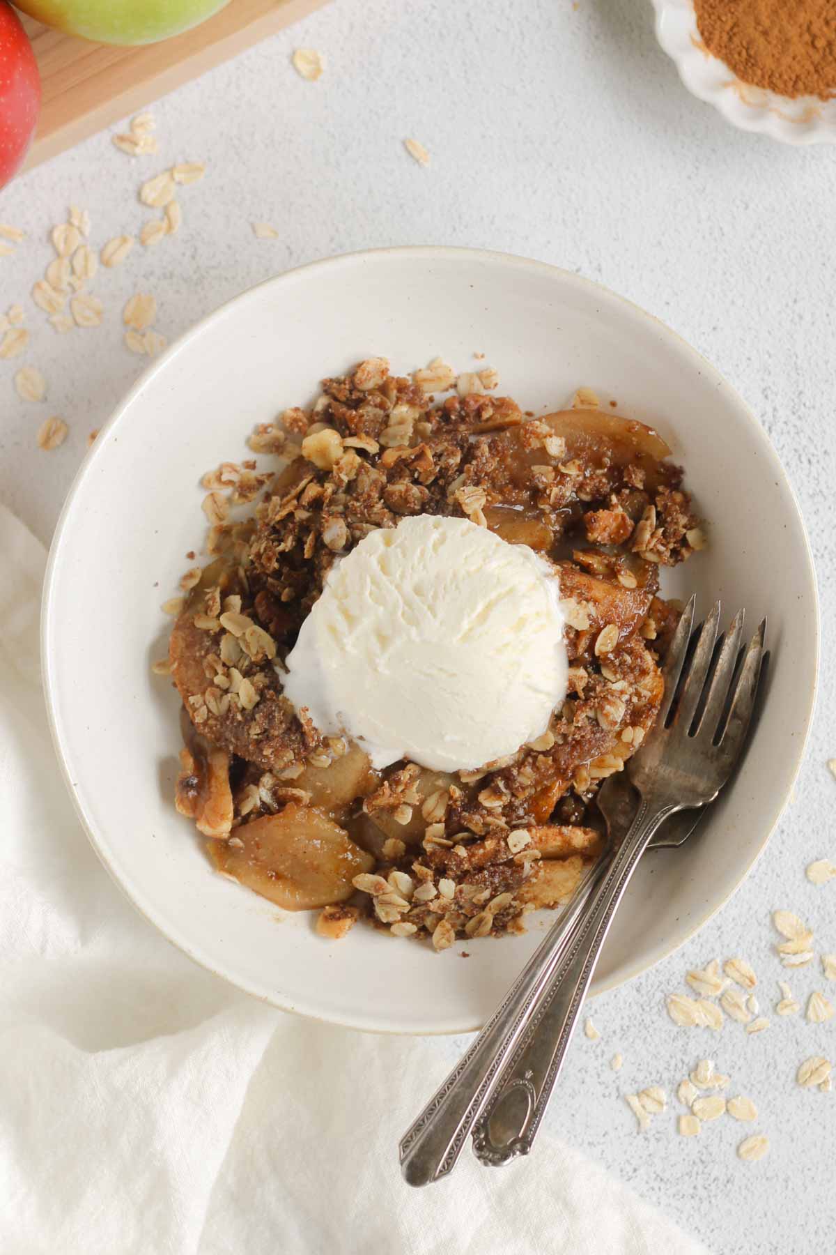 Apple crisp topped with a scoop of ice cream in a small bowl with two vintage forks in the bowl.