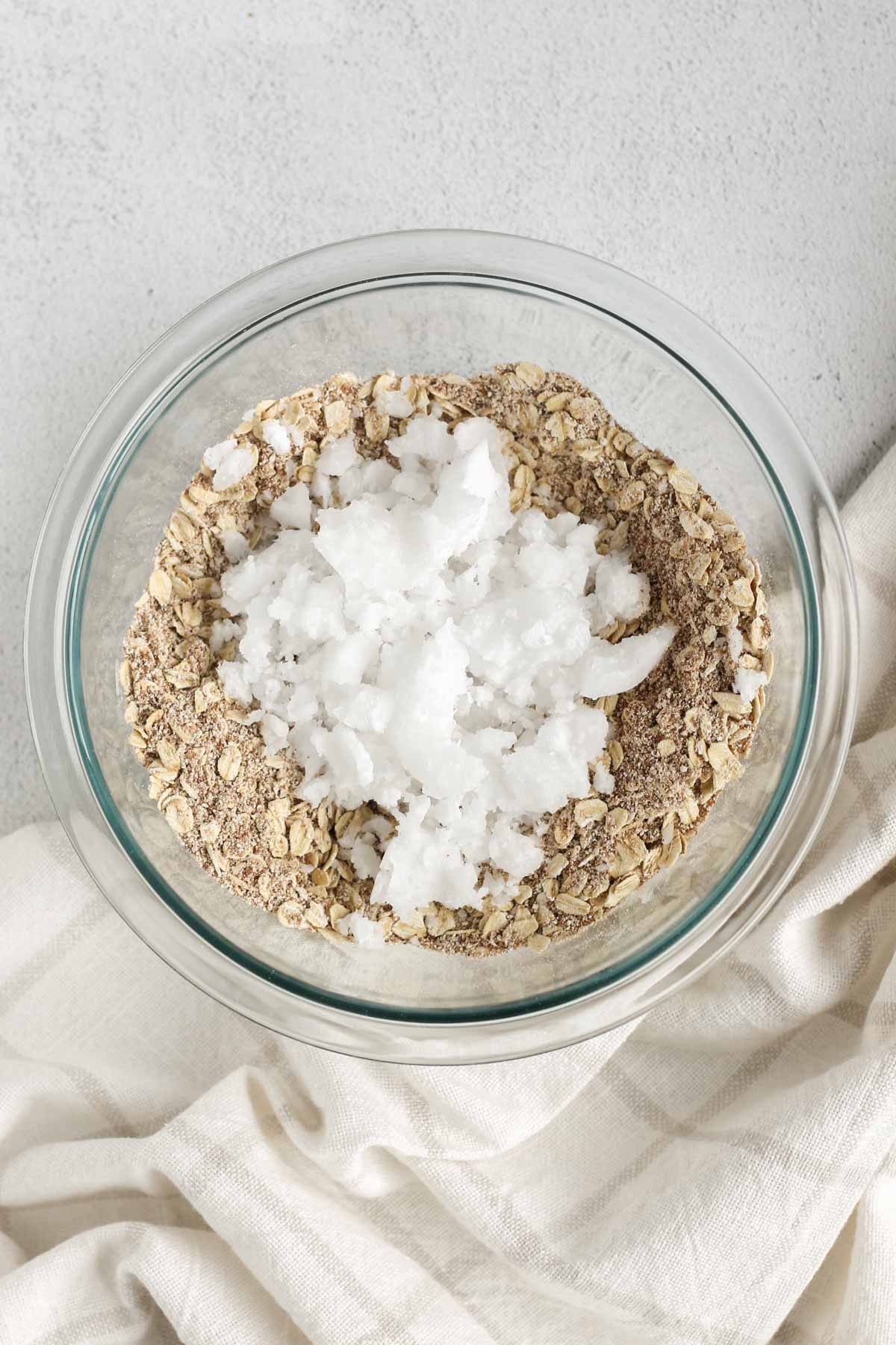 Apple crisp topping mix with pieces of coconut oil on the top in a glass mixing bowl.
