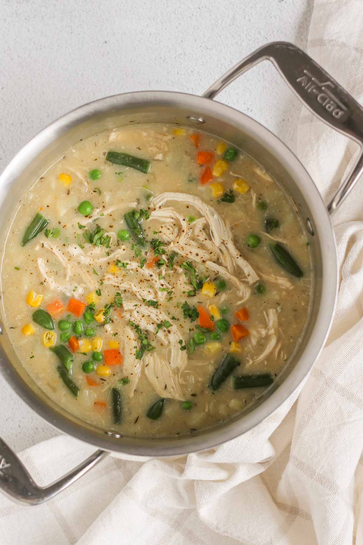 Finished creamy chicken pot pie soup topped with cracked pepper in a stainless steel stock pot.