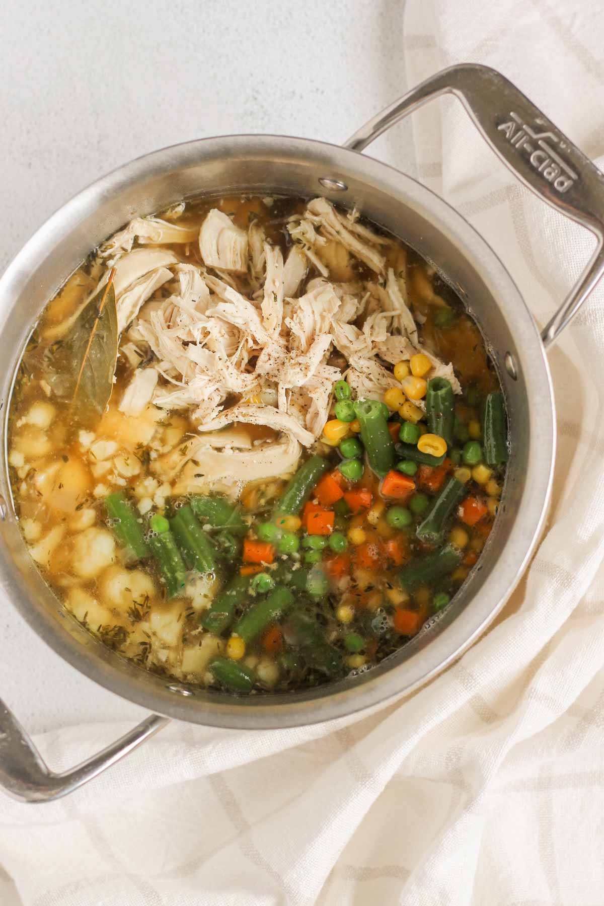 Broth with shredded chicken, cooked cauliflower and frozen mixed vegetables in a stock pot.