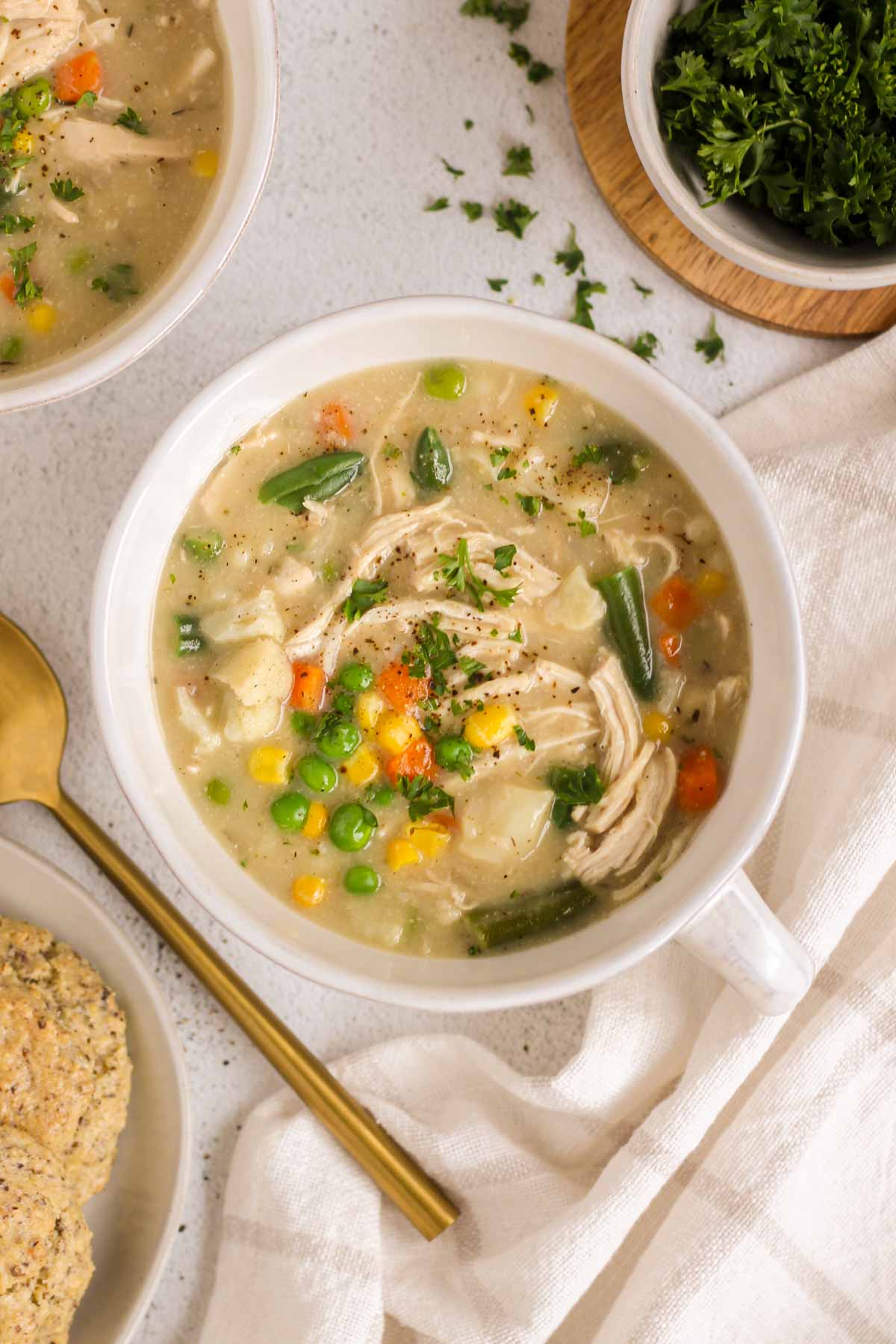 Single serving bowl filled with chicken pot pie soup with a second bowl and a plate of biscuits off to the side.