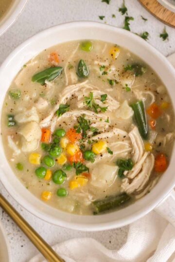 Bowl of creamy chicken pot pie soup with a gold spoon on the side.
