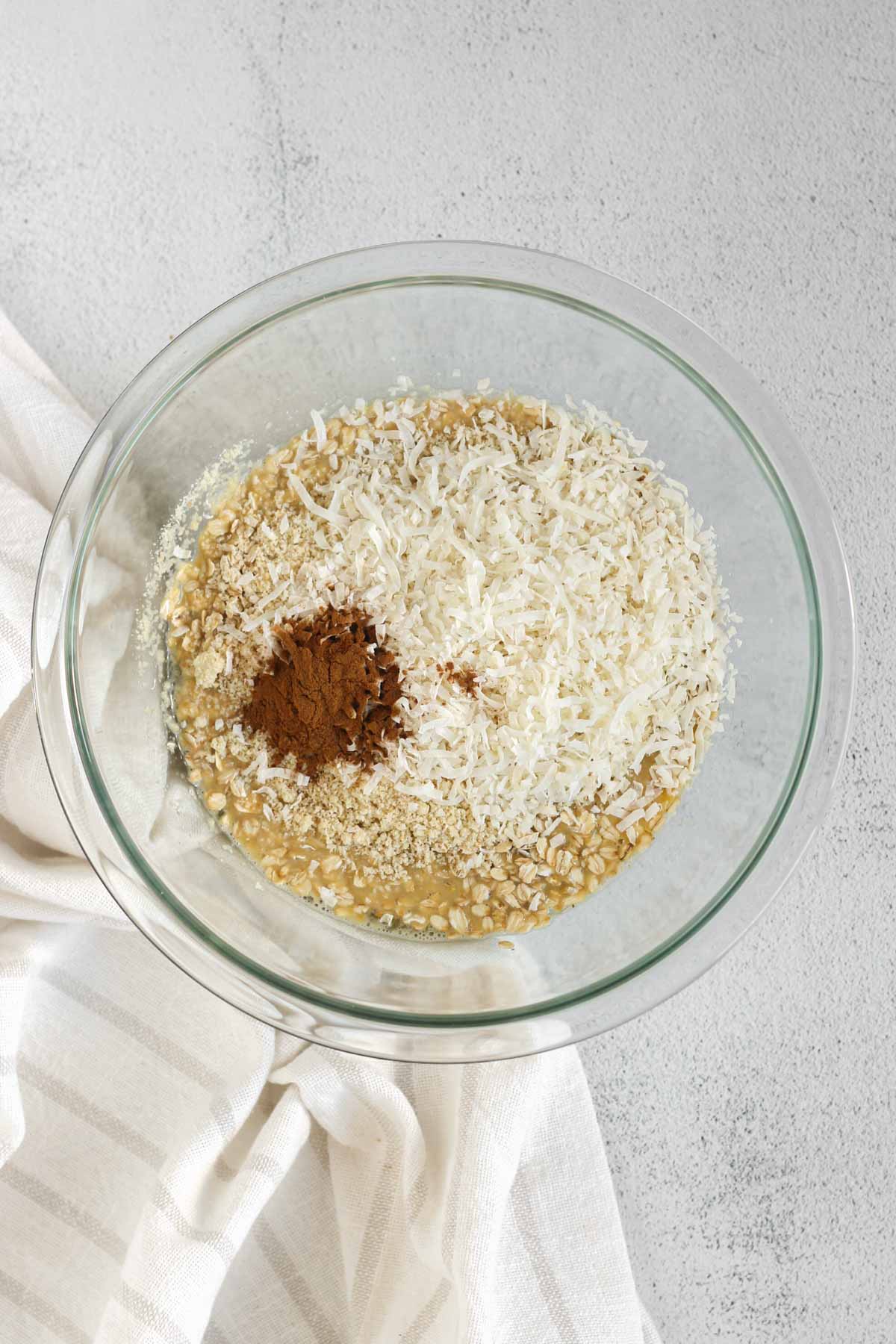 Whisked eggs and milk with oats, cinnamon, coconut and almond flour added to the top, all in a glass mixing bowl.