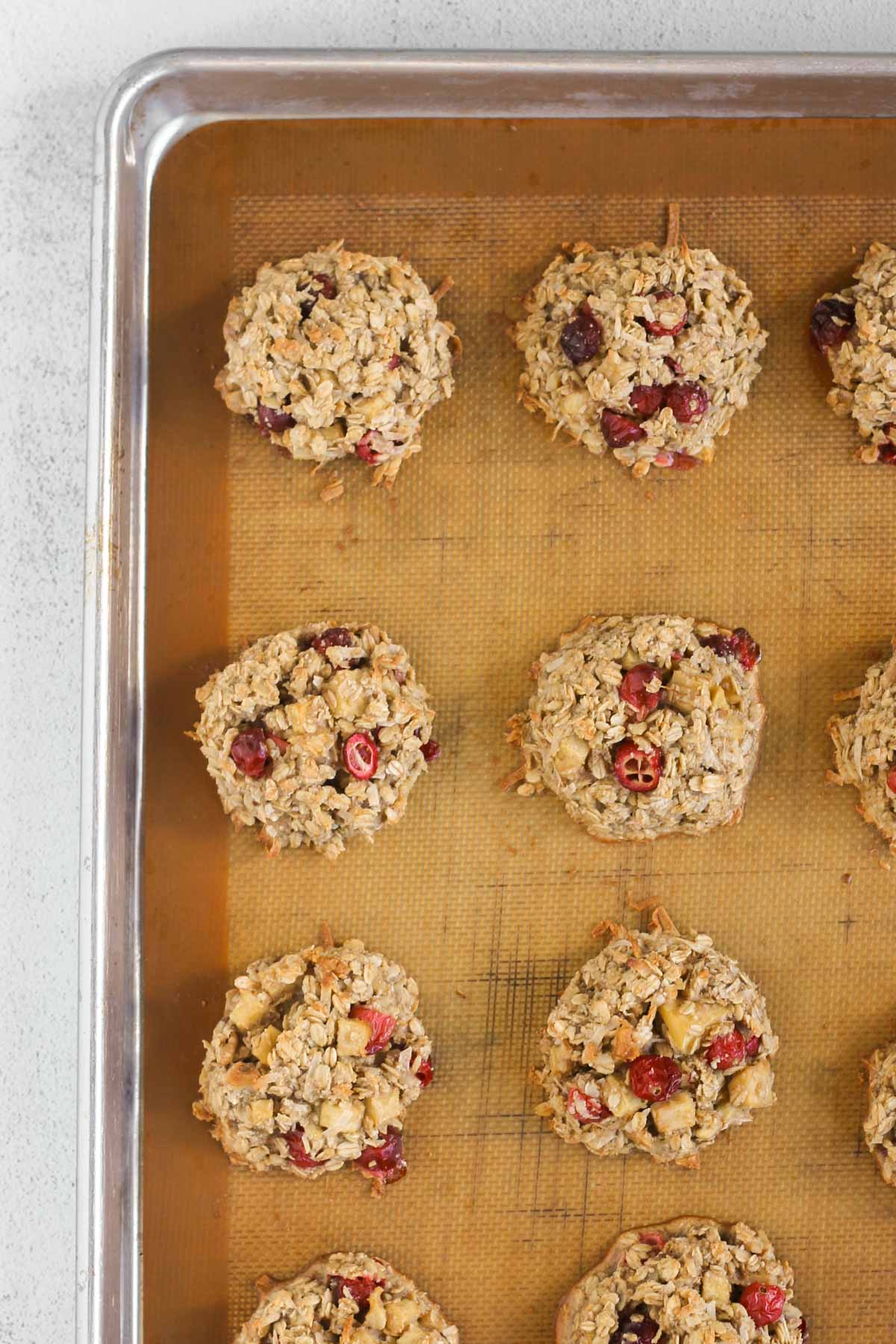 Cranberry apple breakfast cookies baked on a cookie sheet lined with a silicone baking mat.