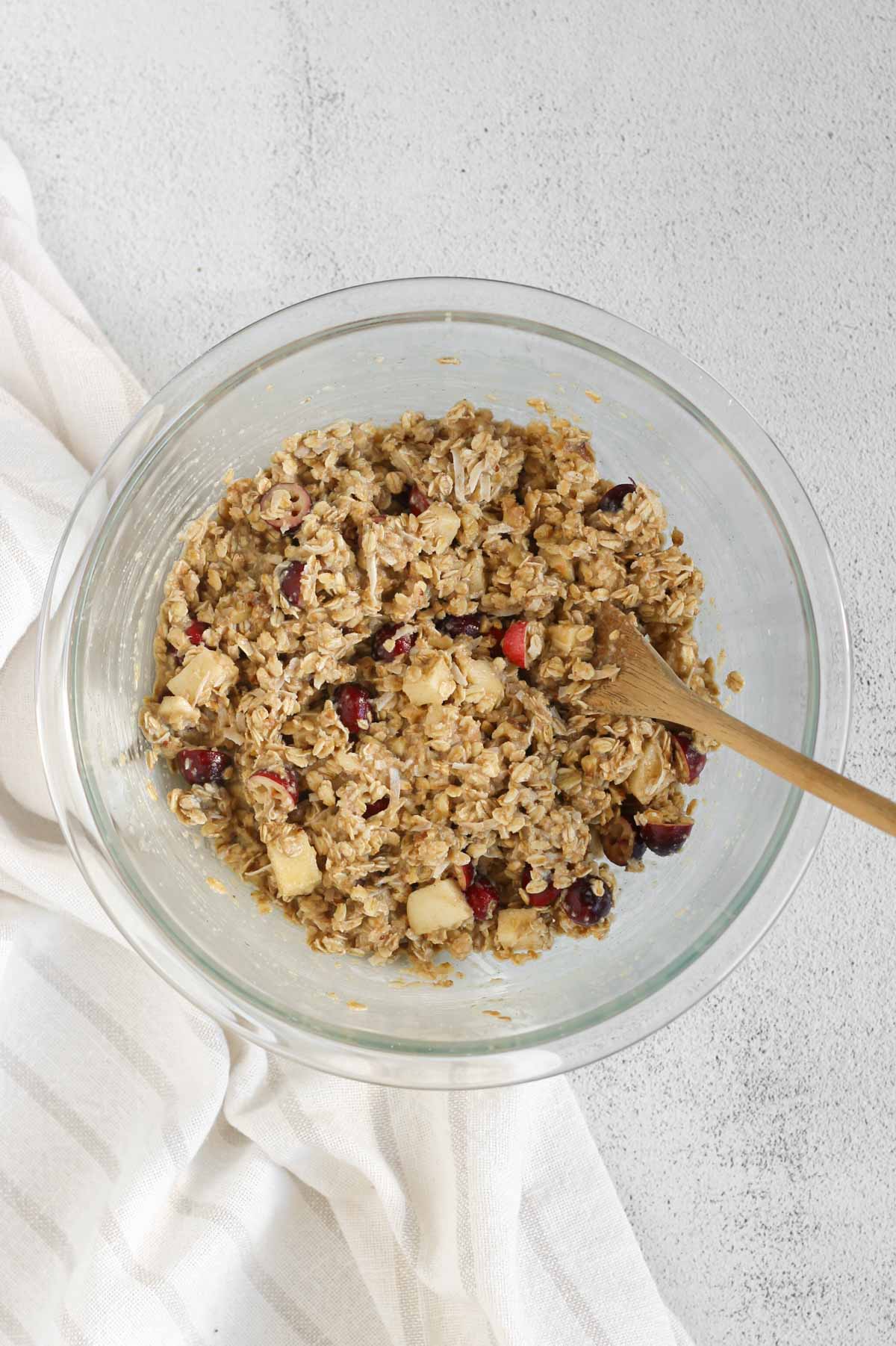 Cranberry apple breakfast cookie ingredients all mixed in a glass mixing bowl with a wooden spoon.