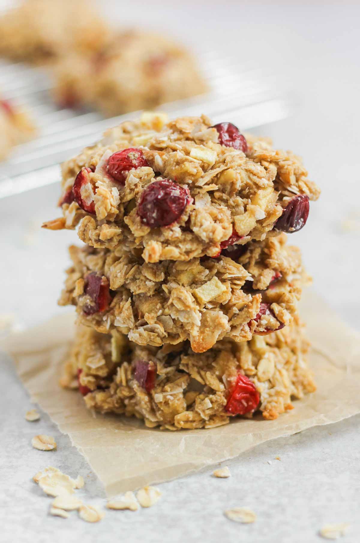 Three cranberry apple oatmeal breakfast cookies stacked on top of each other on a square piece of parchment paper.