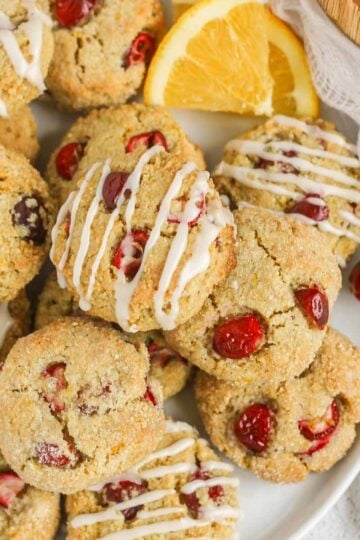 Cranberry almond flour cookies on a plate, so drizzled in icing and some topped with sugar.
