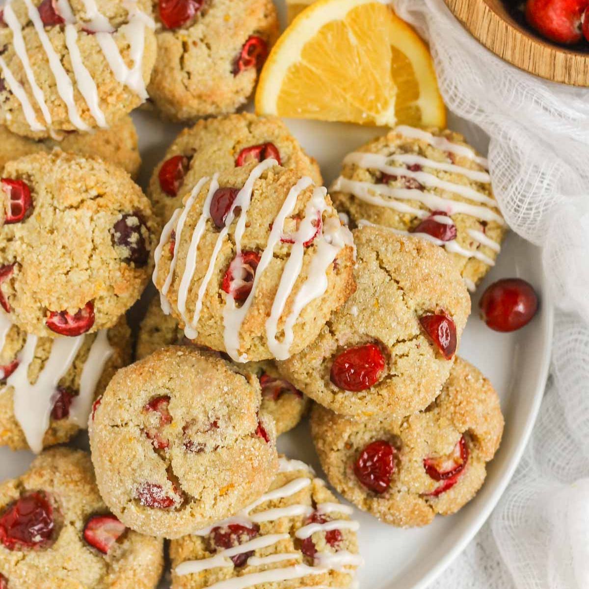 Cranberry almond flour cookies on a plate, so drizzled in icing and some topped with sugar.