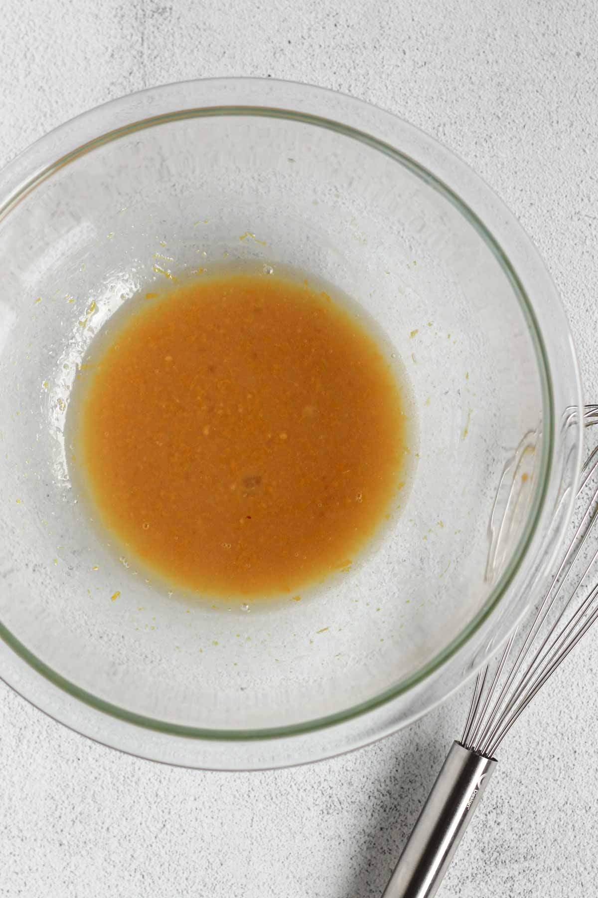 Eggs, coconut oil, orange zest, and maple syrup mixed in a glass mixing bowl with a wire whisk on the side.