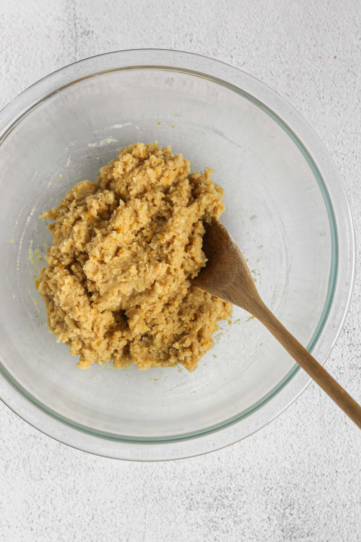 Almond flour cookie dough in a glass mixing bowl with a wooden spoon.