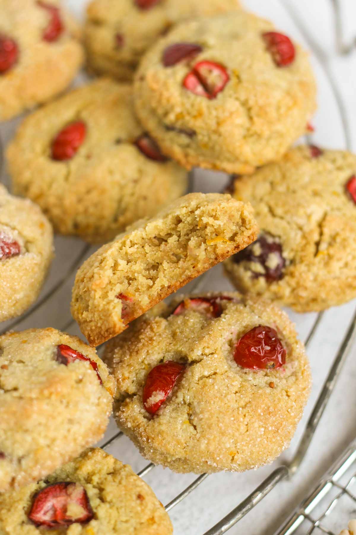 Almond flour cranberry cookies on a cooling rack with a bit taken from one of them to show texture.