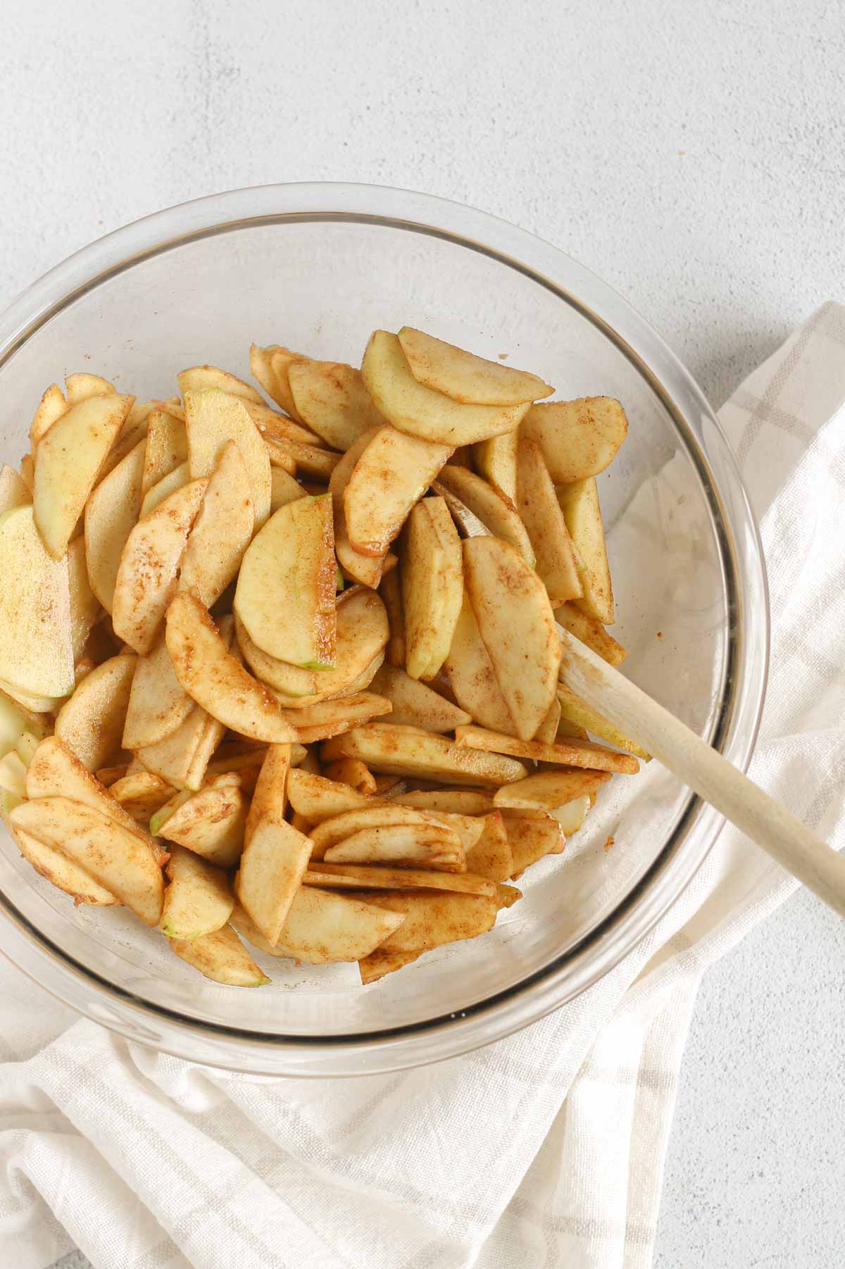 Sliced apples mixed with cinnamon and sugar in a large glass mixing bowl.