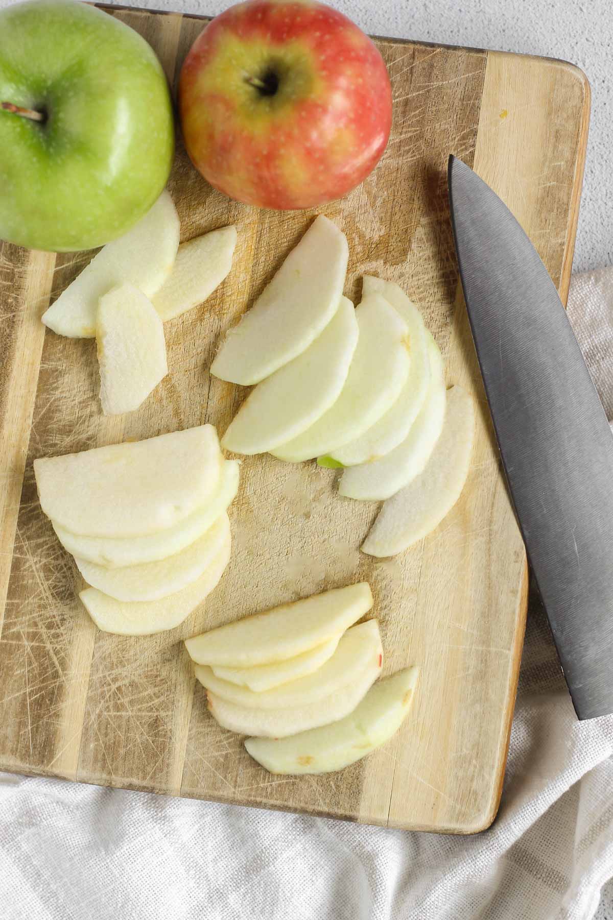 Apple slices and whole apples on a wood cutting board with a large chopping knife.