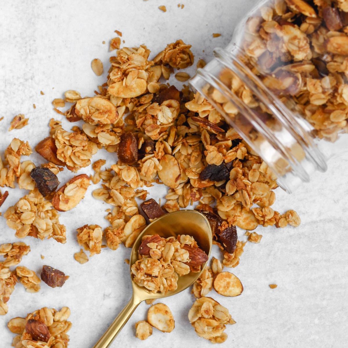 Oats and honey granola spilled from a mason jar with a gold spoon in the spilled granola.