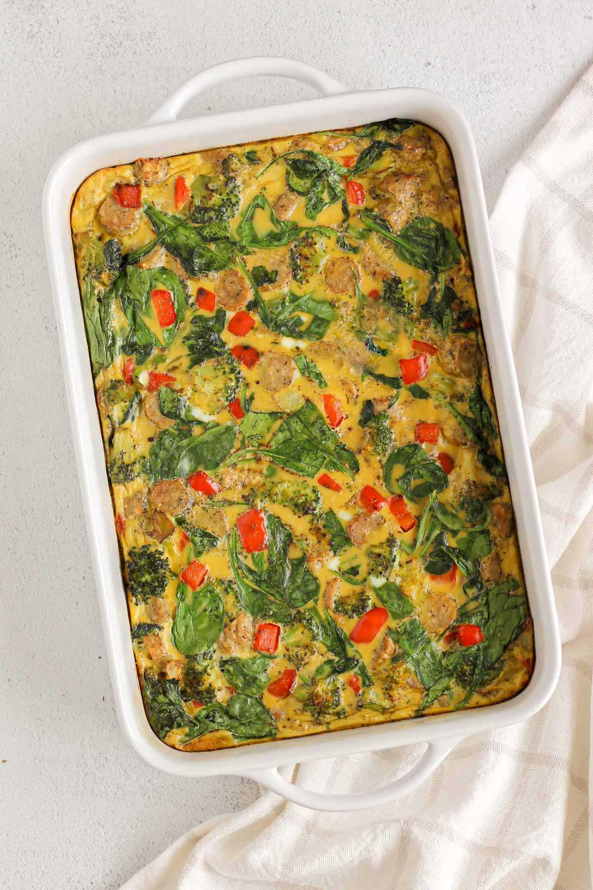 Baked breakfast casserole with spinach, broccoli, red peppers and sliced sausage in a 9x13 casserole dish.