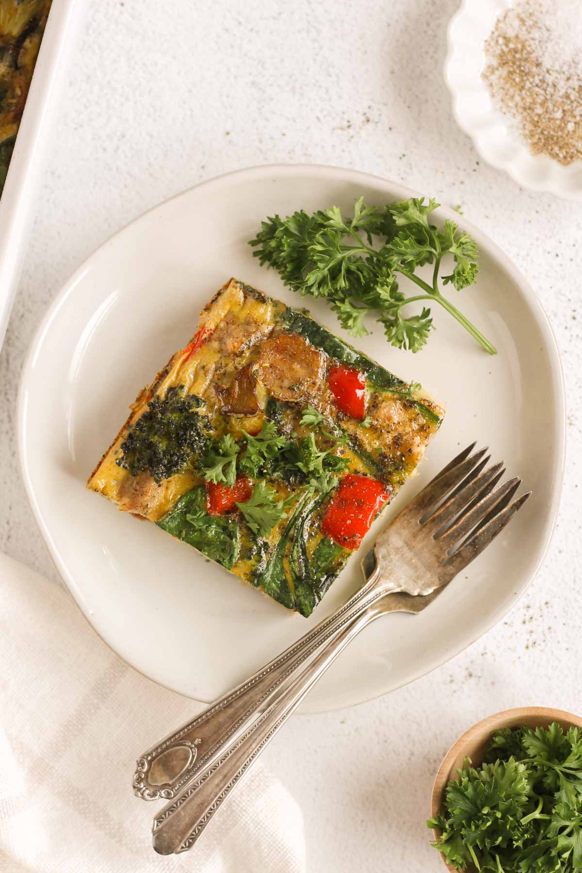 Single piece of dairy-free breakfast casserole with parsley on the side on a small plate with 2 vintage forks.