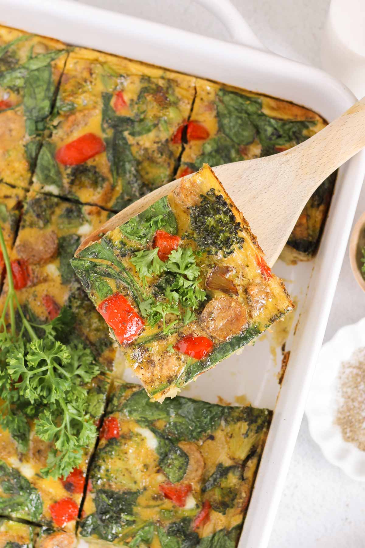 Individual piece of dairy-free breakfast casserole with vegetable and sausage being served from a dish of breakfast casserole.